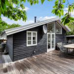 Holzhaus mit Terrasse, Tisch, Stühlen und Grillplatz im Freien.