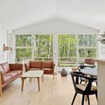 Wohn- und Essbereich mit braunen Ledersofas, Holzmöbeln und Blick auf Wald.