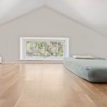 Schlafzimmer mit Holzboden, Fenster und Matratze.