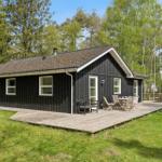 Schwarzes Holzhaus mit Terrasse und Garten. Holztisch, Stühle und Grill sind vorhanden.