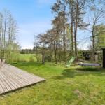 Hinterhof mit Terrasse, Trampolin und Schaukel. Grünfläche und Bäume umgeben die Hütte.