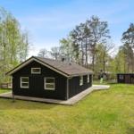 Holzhaus mit Terrasse im Grünen. Gartenbereich mit Spielplatz und kleinem Nebengebäude.
