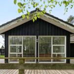 Holzhaus mit großer Fensterfront und Holzterrasse im Wald.