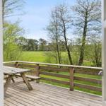 Holzterrasse mit Picknicktisch und Blick auf grünes Feld und Bäume.
