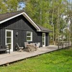 Schwarzes Holzhaus mit Terrasse, Garten und Bäumen im Hintergrund.