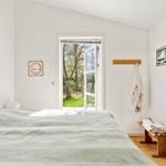 Schlafzimmer mit Bett, Fenster zur grünen Außenseite und Holzbank mit Handtüchern.