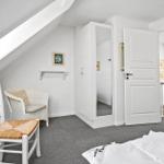 Schlafzimmer mit Dachschrägen, weißer Tür, Kleiderschrank und Stuhl.