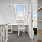 Dachgeschosszimmer mit Schreibtisch, Fenster und Bett im Hintergrund.