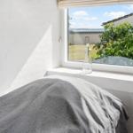 A bed with gray bedding in front of a window overlooking a garden.