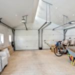 Garage with two doors, bicycle, wheelbarrow, and woodpile. Wall with windows and seating.