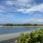 Sea with island and green landscape under blue sky with white clouds.