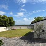 White house with garden, wall, and sea view under blue sky.