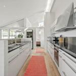 Kitchen with white cabinets, stainless steel backsplash, and red rug on wooden floor