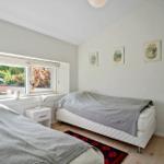Two beds with gray blankets, window with garden view, wall with three pictures.