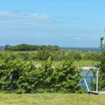 Green slope with view of the sea and an island in the background.