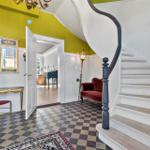 Eingangsbereich mit Wendeltreppe, goldener Konsole und rotem Sessel.