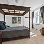 Schlafzimmer mit massivem Bett, Holzboden und Fenster mit Vorhängen.