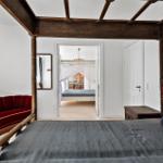 Schlafzimmer mit vierpostigen Bett, rotem Sofa und Blick in angrenzenden Raum.