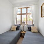 Zwei Betten mit Kissen stehen vor einem Fenster mit weißen Vorhängen.