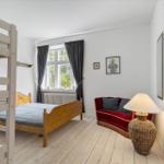 Zimmer mit Doppelbett, Etagenbett und rotem Sofa. Holzboden und Fenster mit Vorhängen.