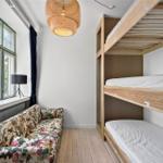 Zimmer mit Schlafcouch, Doppelstockbett und Fenster mit Blick auf Grün.