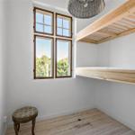 Ein Raum mit Holzboden, Fenster und erhöhtem Bett. Ein Stuhl steht daneben.