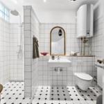 Badezimmer mit Dusche, Waschbecken und Toilette. Weiße Fliesen und schwarz-weiße Bodenfliesen.