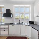 Küche mit weißen Schränken, dunklem Arbeitsplatz und großen Fenstern.
