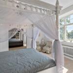 Schlafzimmer mit Baldachinbett, großen Fenstern und Holzboden.