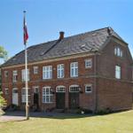 Zweistöckiges Backsteinhaus mit Flagge, Fenstern und Garten.