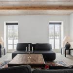 Wohnzimmer mit dunklem Sofa, Holztisch und Fenstern. Decke mit Holzbalken.