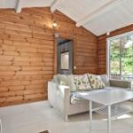 Wohnzimmer mit Holzwand, Sofa und Tisch. Durchgang zur Küche. Fenster zur Terrasse.