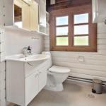 Badezimmer mit Waschbecken, Toilette und Fenster. Wände aus Holz und weiße Möbel.