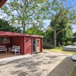 Roter Holzaufbau mit weißen Bänken und Terrasse unter Bäumen.