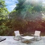 Terrasse mit zwei weißen Stühlen und Tisch, umgeben von Bäumen und Sonnenlicht.