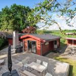 Rotes Holzhaus mit Terrasse, Grill und Schaukel im Grünen.