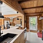 Küche mit Arbeitsplatte, Spüle und Dunstabzug. Holzwände und Deckenbalken. Tür zum Garten.