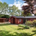 Rotes Holzhaus mit Garten, Terrasse und Grillplatz unter Bäumen.