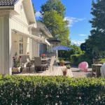 Terrasse mit Tisch, Stühlen und Sonnenschirm neben einem Haus mit Balkon.