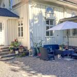 Haus mit Terrasse, Sitzgruppe und Sonnenschirm. Pflanzen und Steine dekorieren den Außenbereich.