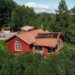 Rotes Holzhaus mit Solaranlage, umgeben von Wald und Grünfläche.