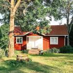 Rotes Holzhaus mit weißen Fenstern und Tür, umgeben von Bäumen und Gras.