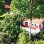 Rotes Haus mit weißen Fenstern und Veranda, umgeben von grünen Bäumen und Rasen.