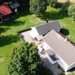 Haus mit Garten, Terrasse und rotem Schuppen. Umgeben von Bäumen und Gras.