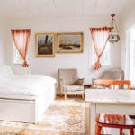 Ein Schlafzimmer mit Bett, Stühlen und Wandbildern. Fenster mit roten Vorhängen.