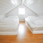 Zwei Matratzen mit weißen Bettwäschen in einem Dachbodenzimmer mit Holzboden und Fenster.
