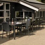 Terrasse mit Tisch und Stühlen vor einem Haus mit dunklem Holzschindelverkleidung.