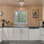 Küche mit weißen Schränken, schwarzer Arbeitsplatte und Holzwand. Fenster mit Blick auf Garten.