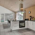 Küche mit weißer Arbeitsplatte und Edelstahlherd. Holzwände und -decke. Blick in Essbereich mit Pool.