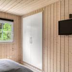 Schlafzimmer mit Holzwand, Fenster, Kleiderschrank und Wandfernseher.